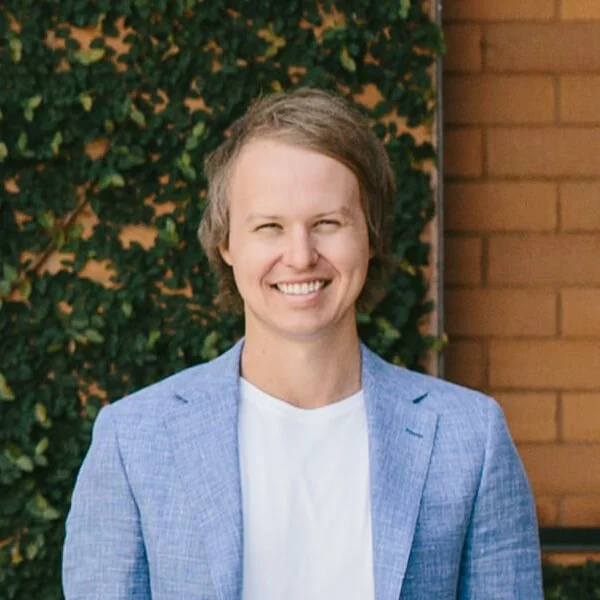 A man in a blue jacket smiling in front of a brick wall.